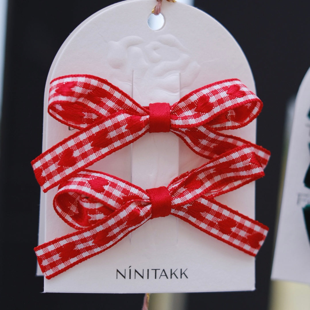 Red gingham bow hair clips featuring sweet heart designs, perfect for a charming and classic look. The checkered pattern brings a delightful, nostalgic feel to any outfit.