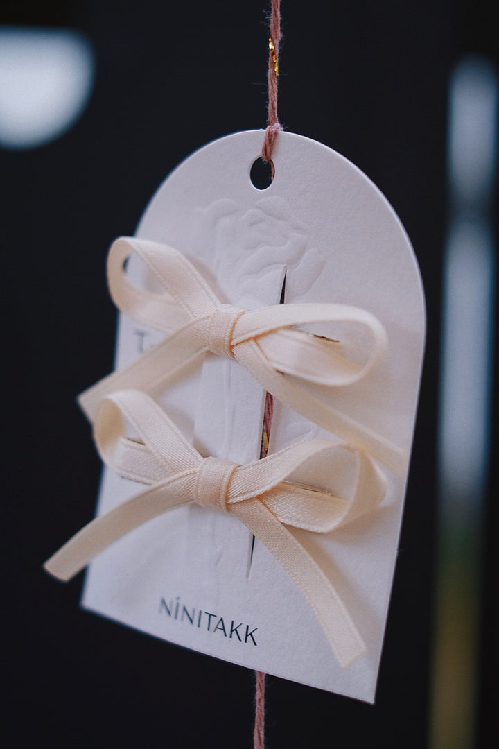 Cream-colored bow hair clips laid out neatly. The soft, neutral hue makes these clips a versatile accessory that can complement any outfit.
