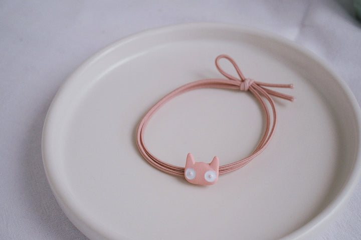 A detailed close-up photograph showcasing one of the hair ties in pink color, highlighting the intricate cat design with its big eyes and pointy ears.