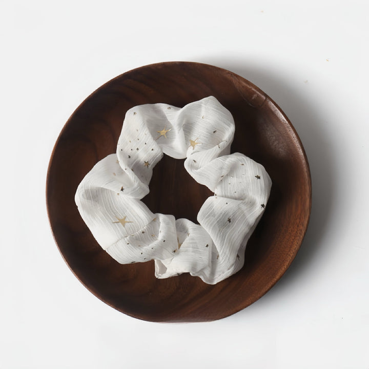 Stay classic with this white scrunchie decorated with golden stars and sparkles, a versatile choice for any outfit.
