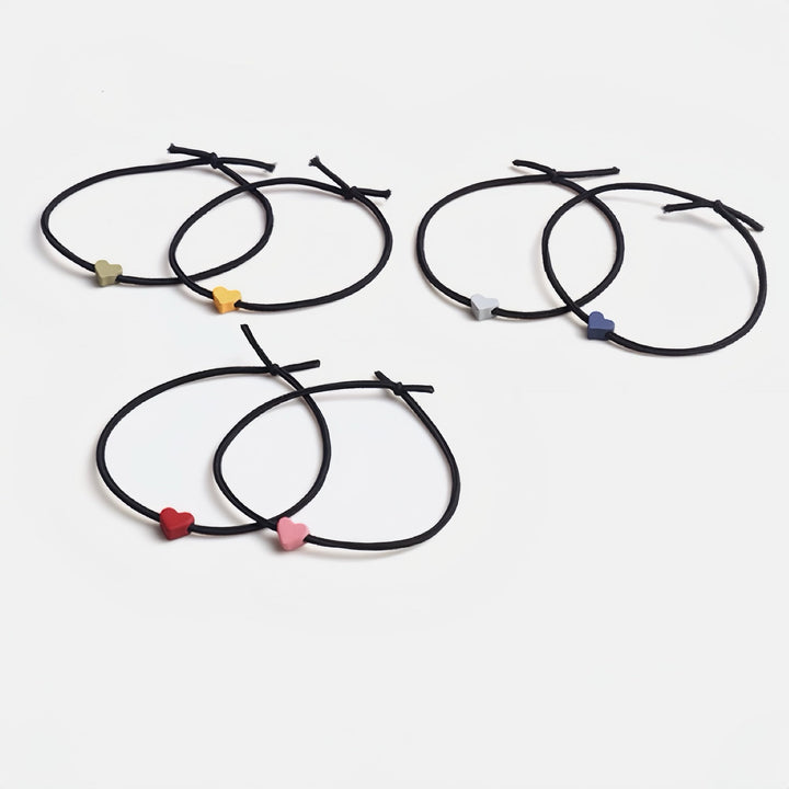 Set of six elastic hair ties, each with a tiny heart in different colors—deep blue, yellow, bright red, pink, light purple, and green—arranged on a white background.