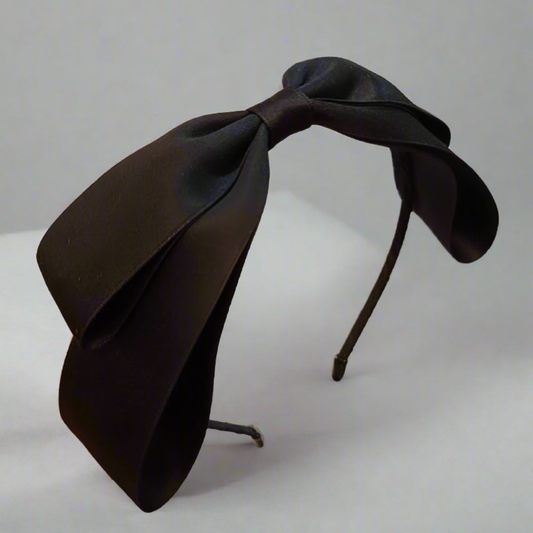 A sleek black headband with a large, luxurious satin bow, perfect for creating a chic and polished look. The bow's generous size, approximately 25 cm, ensures it stands out in any setting.