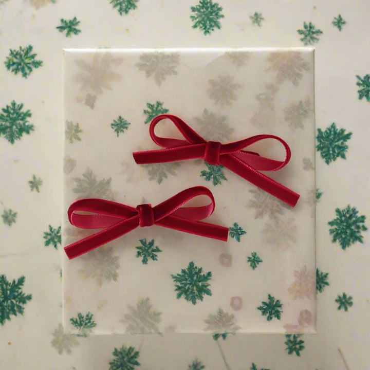 Two vibrant velvet red bow hair clips displayed on a textured surface, showcasing their bright color and sturdy construction, perfect for festive occasions.