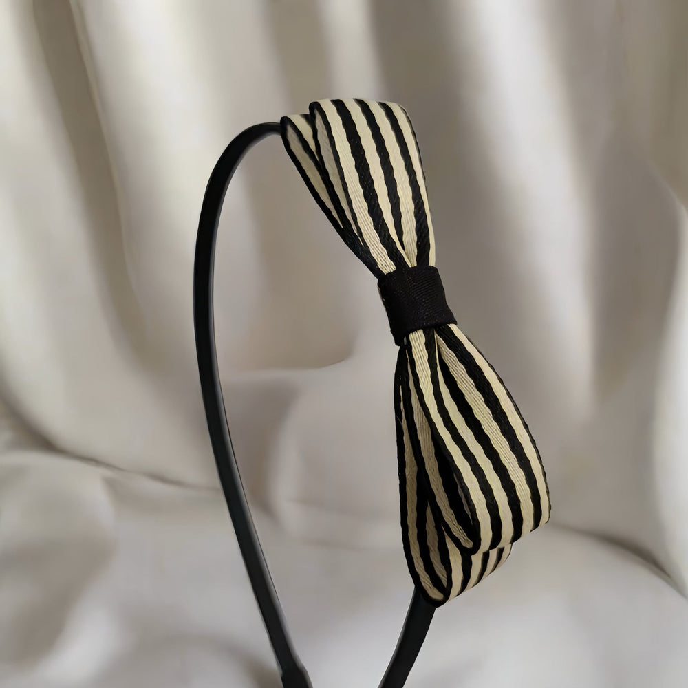 This elegant headband boasts a sophisticated cream and black striped bow, providing a modern twist on a classic design. The 9 cm double-layer fabric bow is perfect for adding a refined touch to any outfit.