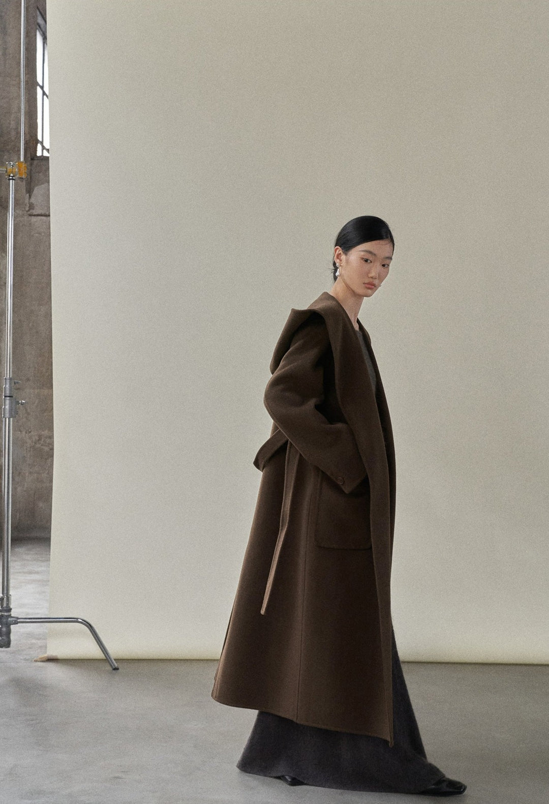 Side view of the model in the chocolate coat, demonstrating its relaxed fit and attached hood.