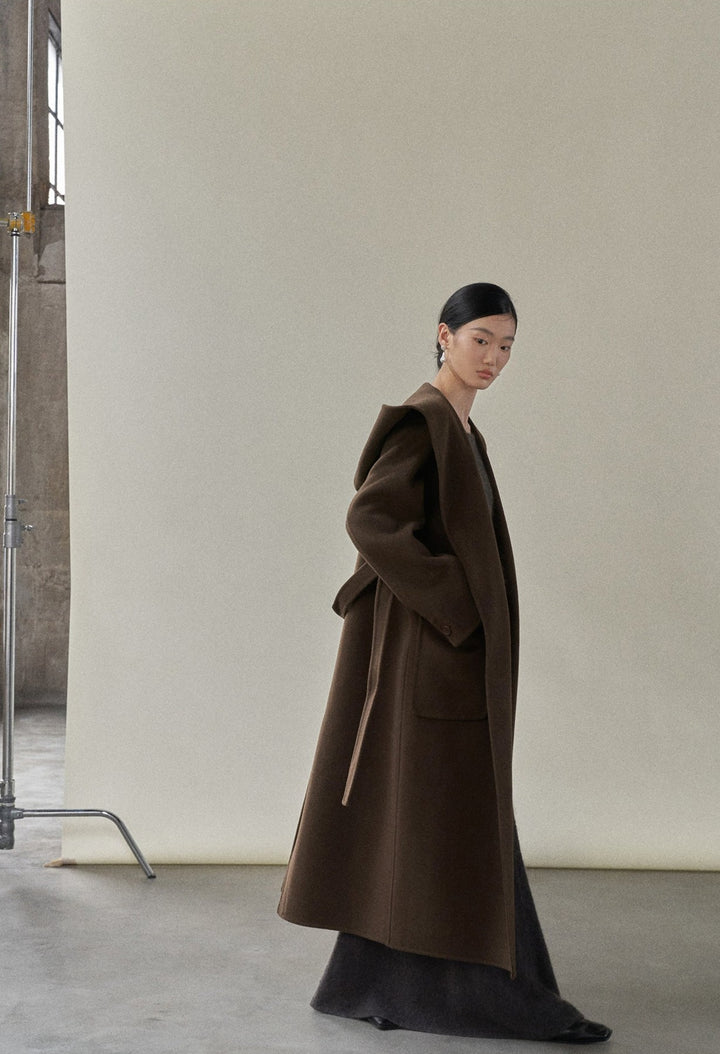 Side view of the model in the chocolate coat, demonstrating its relaxed fit and attached hood.