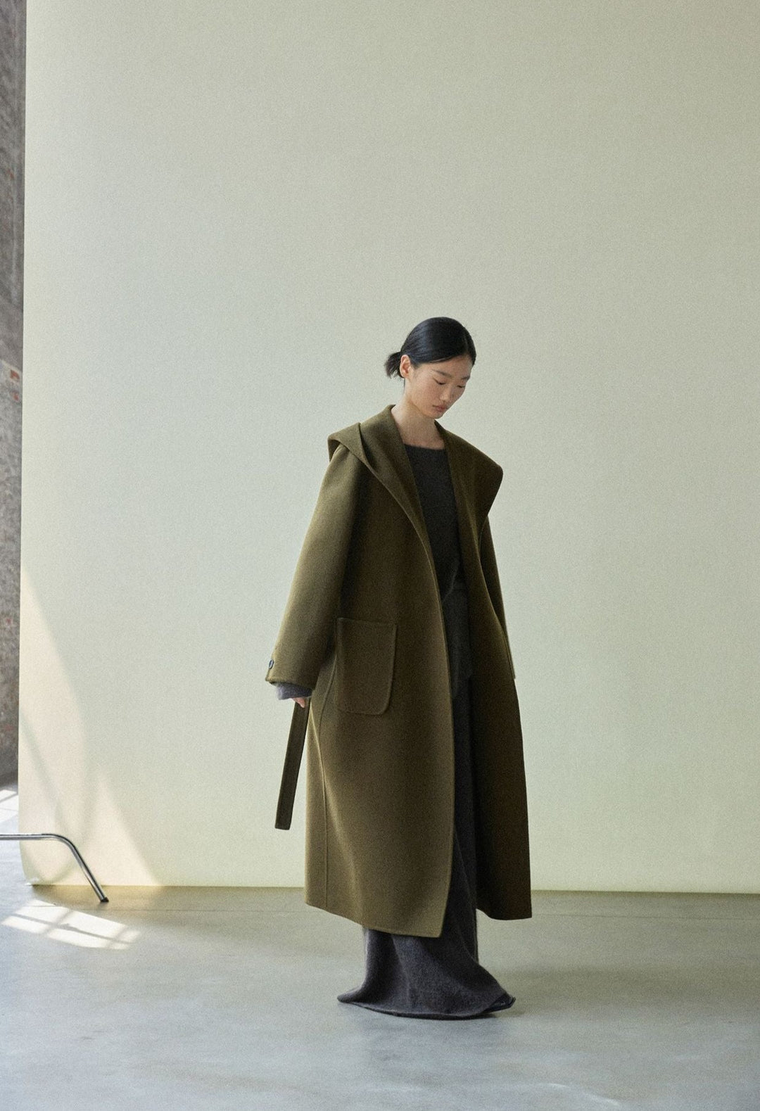Action shot of the model walking in the olive green coat, showcasing its flow and movement.