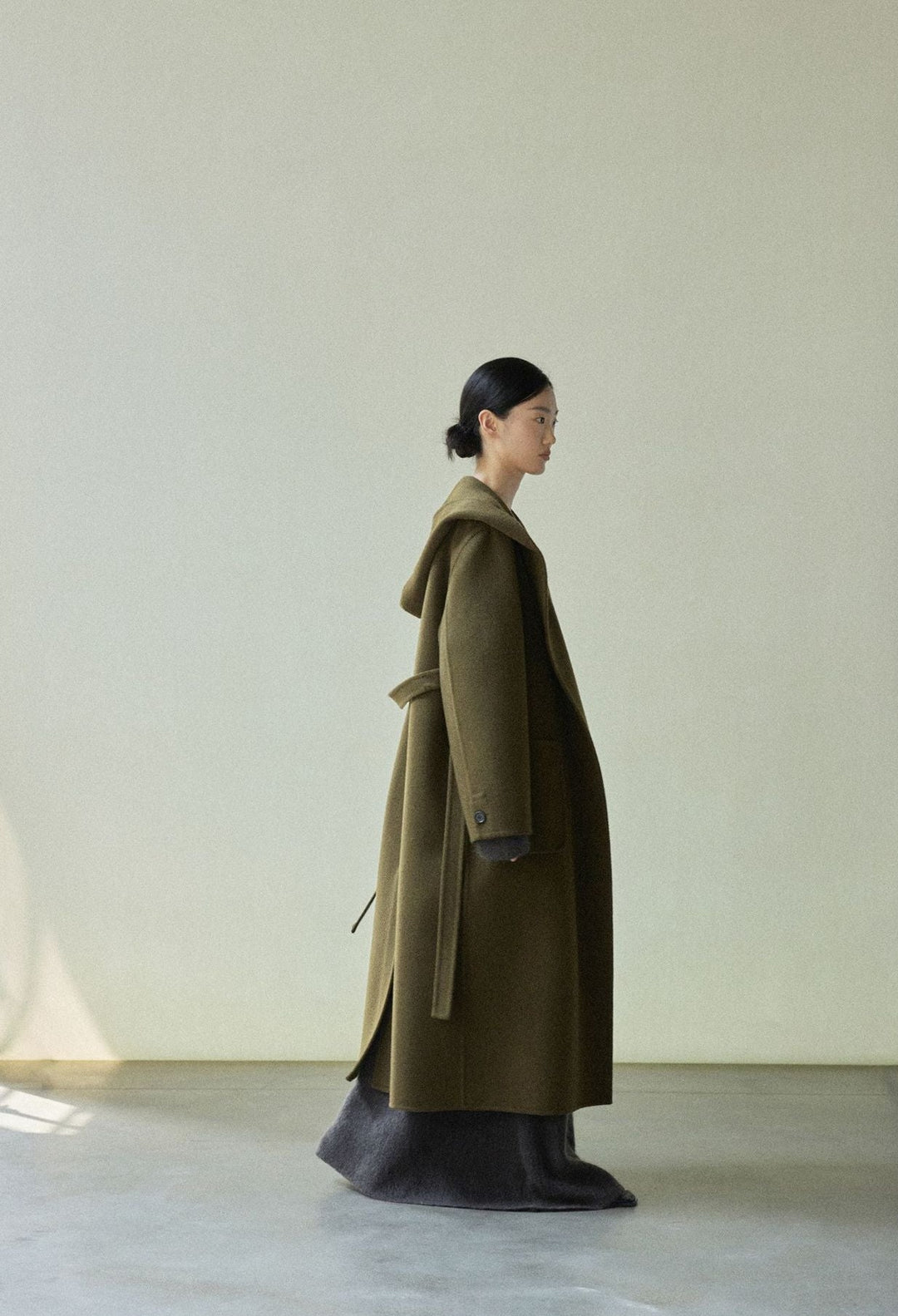 Side view of the olive green coat, highlighting the long length and relaxed fit.