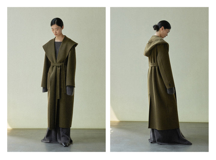 The model stands in the olive green robe coat, showcasing its elegant drape and attached hood.