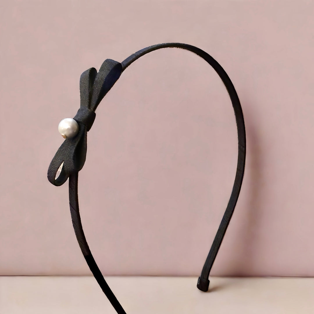 This chic headband highlights a sleek black satin bow accented by a classic pearl, adding a dash of sophistication. The 6 cm bow sits elegantly on a durable iron headband, making it perfect for elevating any ensemble with a touch of grace.