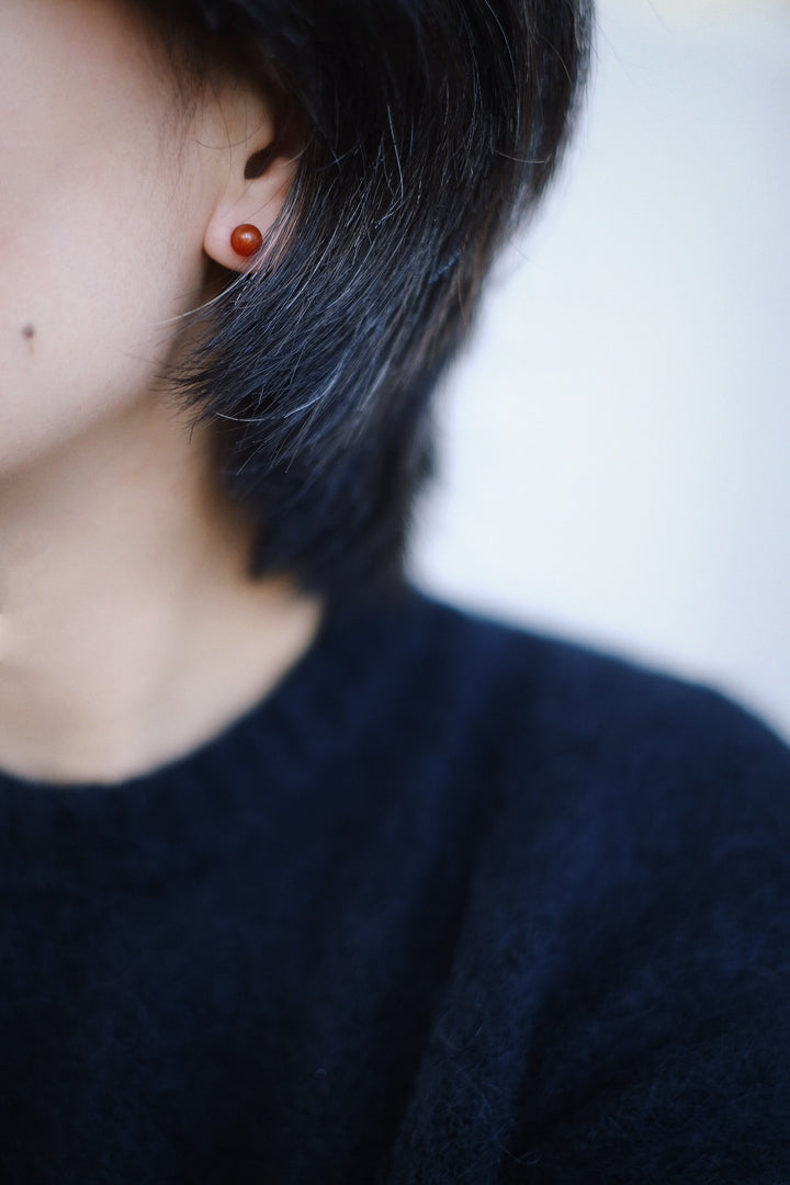 A side profile of a model wearing the 6mm red onyx stud earrings. The deep red color contrasts beautifully with the model's skin tone, adding a touch of elegance to her look.