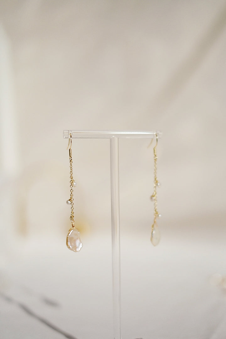 The Enchanted Woodland Hook Earrings rest on a earring stand, emphasizing their intricate design and the shimmering quality of the pearls against the gold-plated setting.