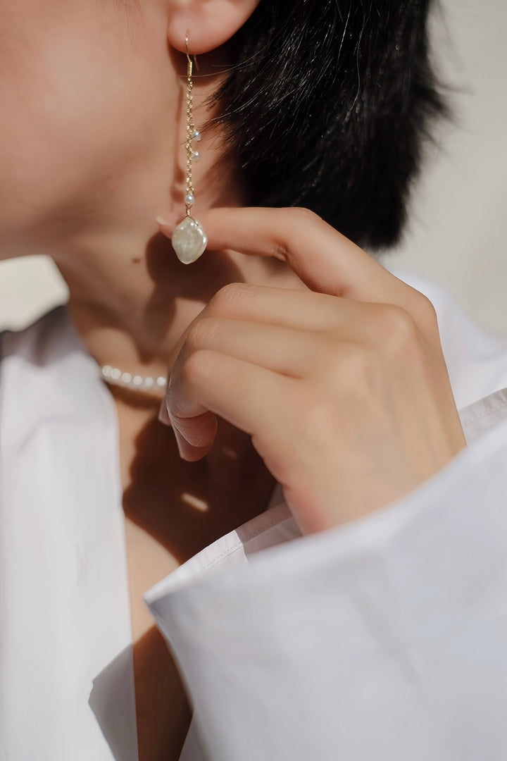 A close-up of a model showcasing the long, delicate Enchanted Woodland Hook Earrings. The earrings dangle elegantly, highlighting the lustrous baroque pearl and three small freshwater pearls.