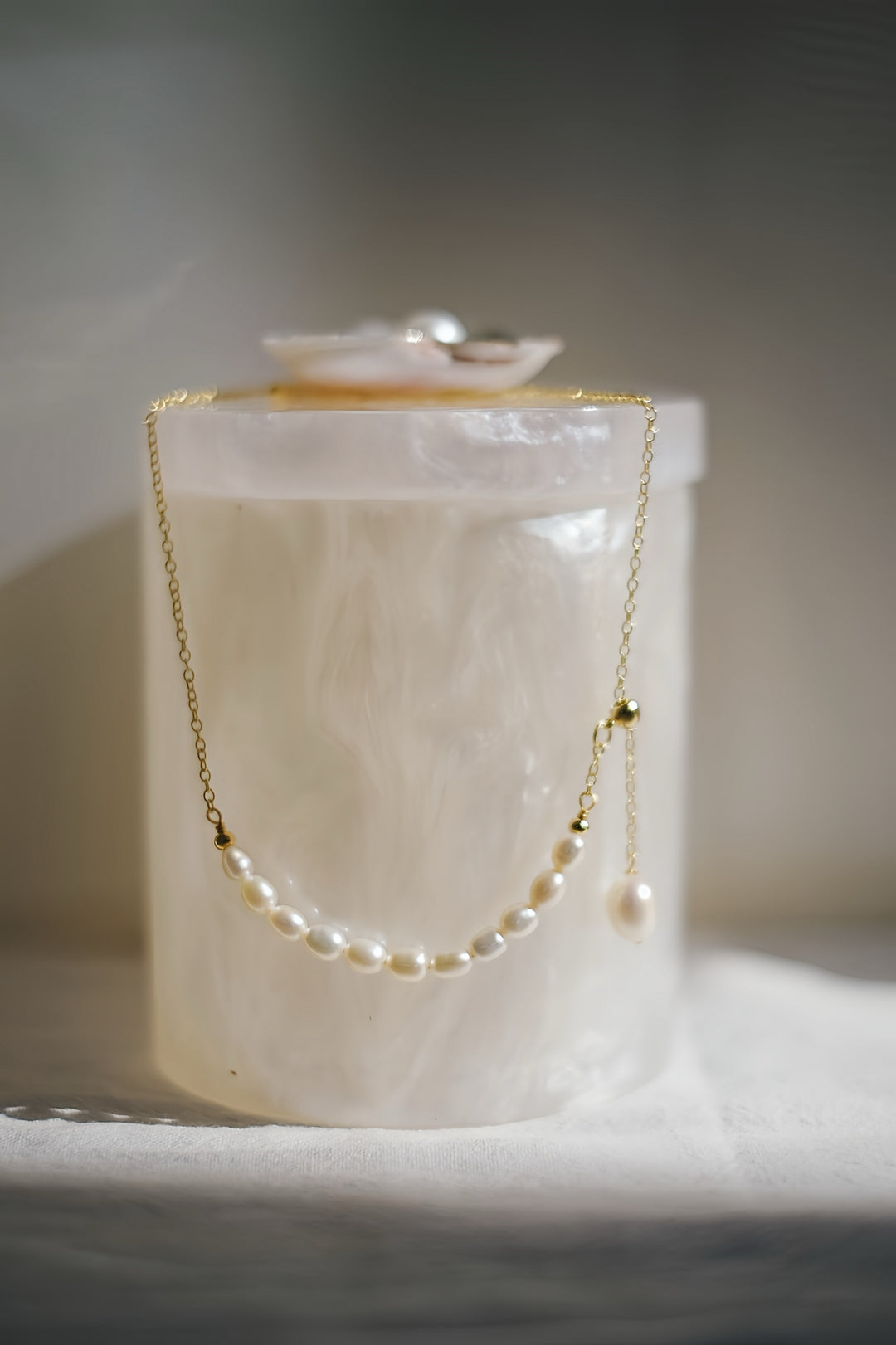 A detailed shot of the necklace laid out, highlighting the asymmetric arrangement of pearls and the elegant drop of the single teardrop pearl. The golden chain glistens softly, adding a touch of modernity to the timeless design.