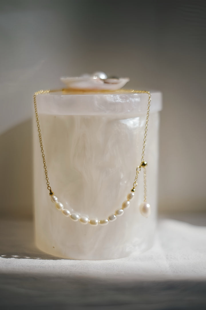 A detailed shot of the necklace laid out, highlighting the asymmetric arrangement of pearls and the elegant drop of the single teardrop pearl. The golden chain glistens softly, adding a touch of modernity to the timeless design.