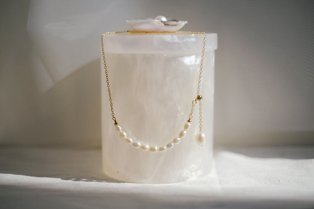 A poetic close-up of the Pearl of the Moonlit Path necklace resting on a soft, alabaster surface. The pearls glow subtly, as if lit by moonlight, with the delicate golden chain enhancing their natural beauty.
