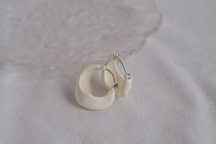 The white wavy hoops are paired with a silver-toned post, complimenting the main color tone.