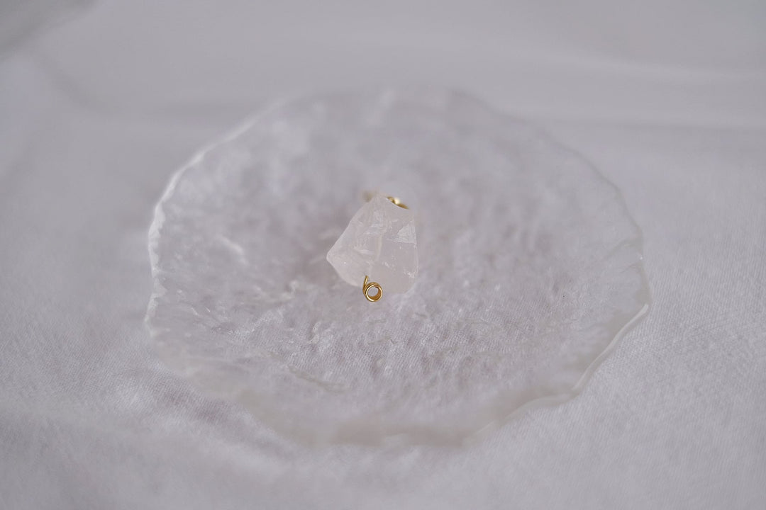 A close-up shot of the white crystal earring, capturing the clarity and brilliance of the clear quartz against the gold setting.