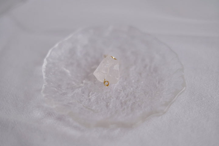 A close-up shot of the white crystal earring, capturing the clarity and brilliance of the clear quartz against the gold setting.