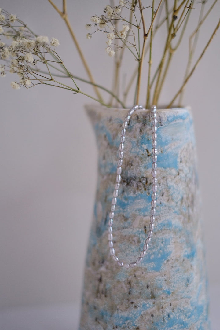 Effortlessly chic, the necklace is draped over a vase, offering a glimpse of its graceful silhouette and lustrous pearls.