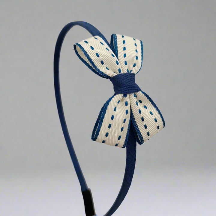 This delightful headband showcases a crisp white bow with charming blue edges and delicate stitches, perfect for adding a refined touch to any look. The small bow, approximately 6 cm, is elegantly crafted, making it ideal for both everyday wear and special events.