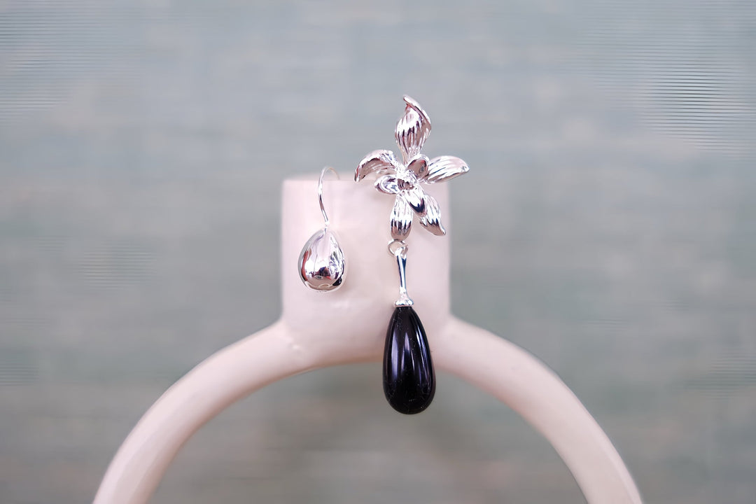 A single Daffodil earring on a minimalist white stand, focusing on the detailed flower design and the smooth, black teardrop bead, capturing its timeless elegance.