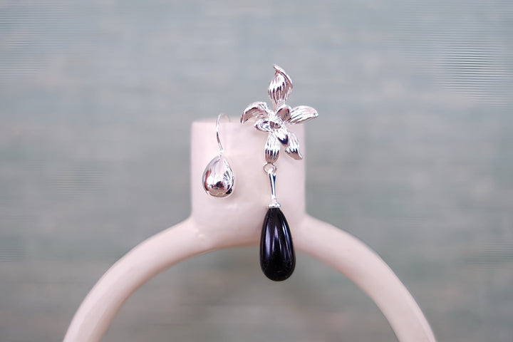 A single Daffodil earring on a minimalist white stand, focusing on the detailed flower design and the smooth, black teardrop bead, capturing its timeless elegance.