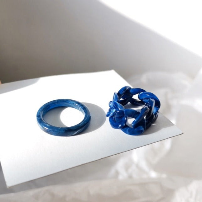 Captured in natural light, this image features the "Frozen Waves" rings on a white surface. The play of light and shadow enhances the depth and richness of the resin colors, bringing out the true beauty of these carefully crafted pieces.