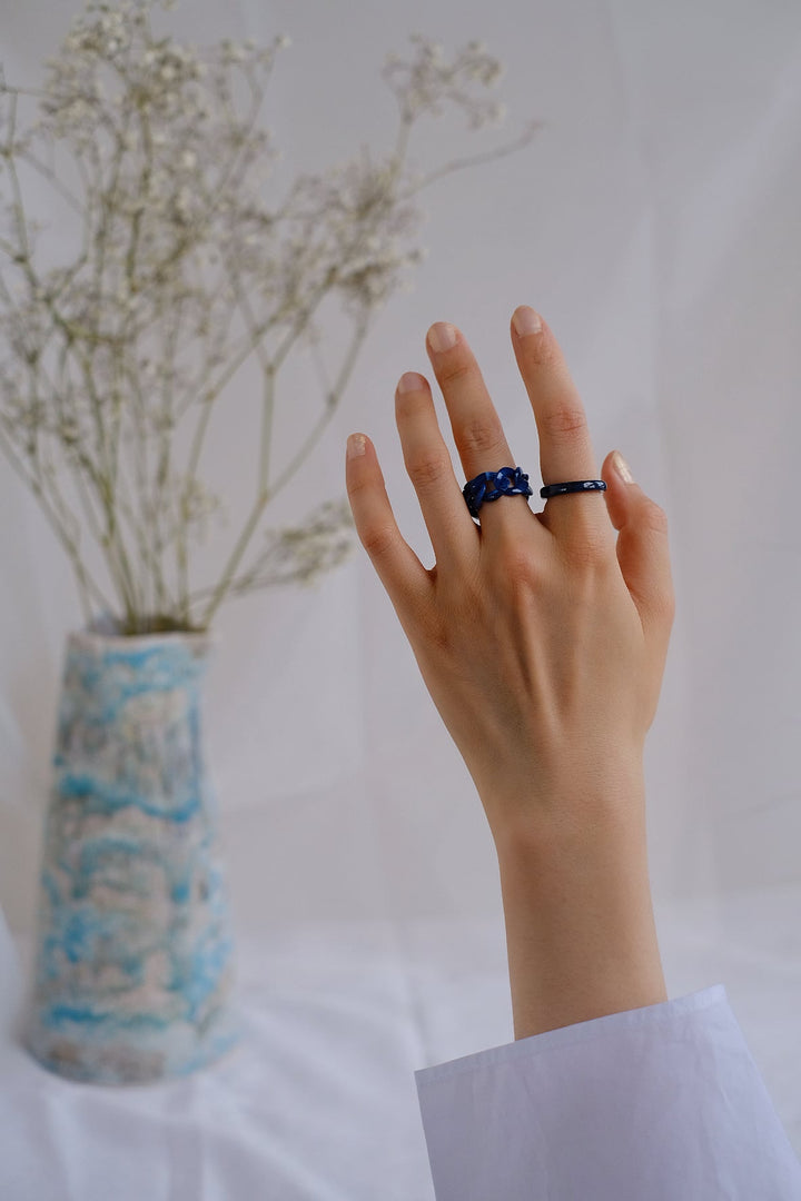 The second image captures the Interwoven Tales rings in the dark blue and light blue option, beautifully worn on a hand. The deep blue band and the delicately interwoven lighter blue ring create a striking contrast, perfect for making a bold statement.