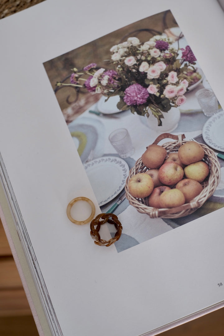 This image displays the "Sand Dunes" rings elegantly placed on a magazine page. The intricate interwoven pattern of the coffee-colored ring and the smooth beige band stand out against the rustic background, highlighting their unique design and complementary colors.