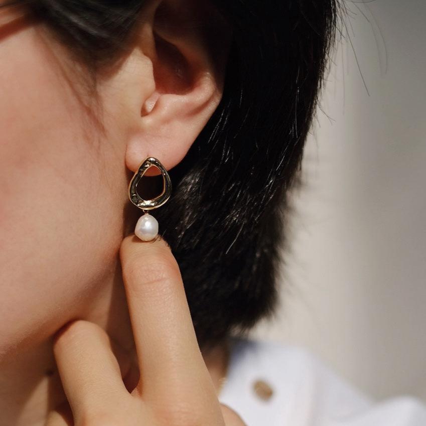 A hand holding one of the earrings, demonstrating the size and intricate details of the design.