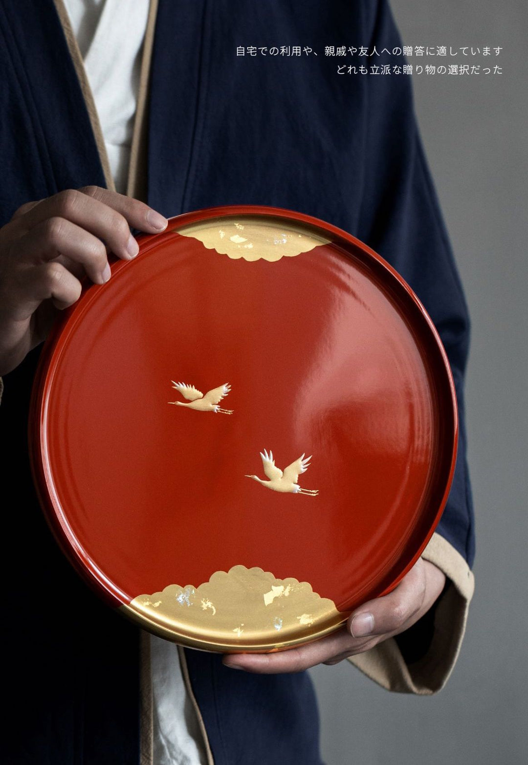 The tray is displayed in hand, showcasing its size and the intricate gold leaf design of cranes and mountains. The deep, glossy finish of the lacquer highlights its luxurious appeal.