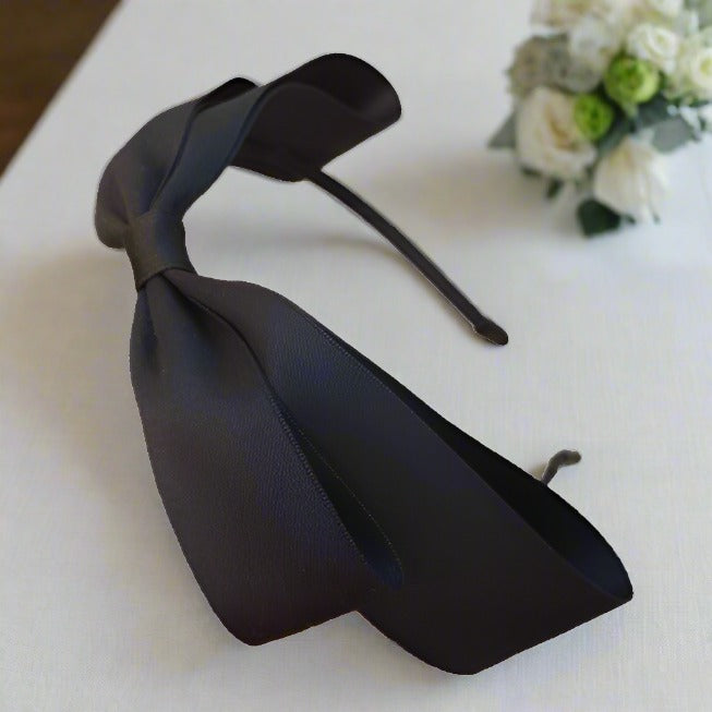 This image highlights the graceful curvature and size of the black satin bow headband, ideal for complementing a variety of outfits with a touch of elegance.