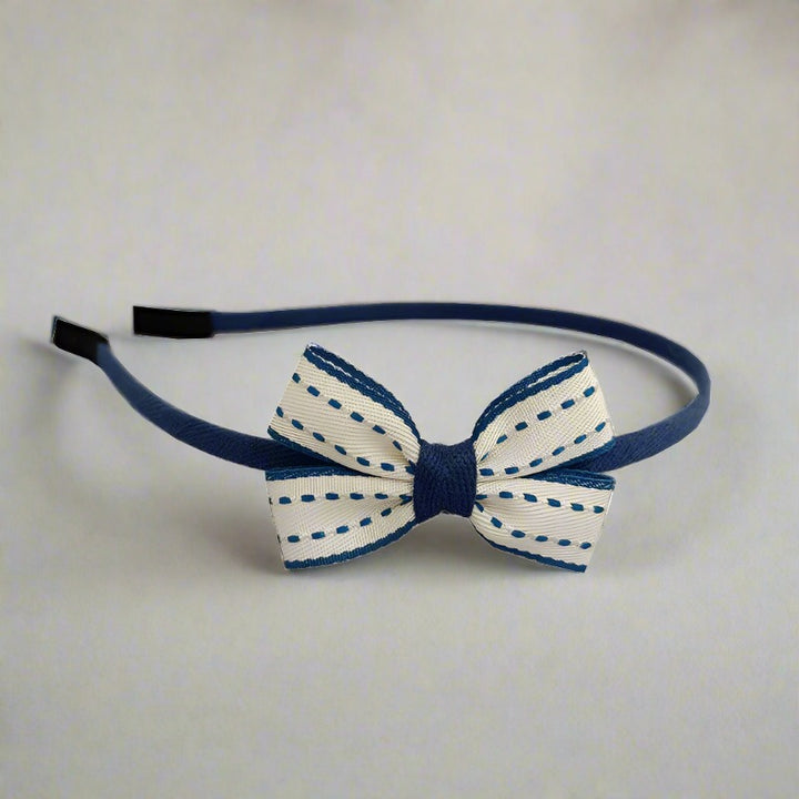 This playful headband features a white bow with charming blue edges and stitches, perfect for adding a fun and whimsical touch to any girl's outfit. The bow's compact size makes it a versatile accessory.