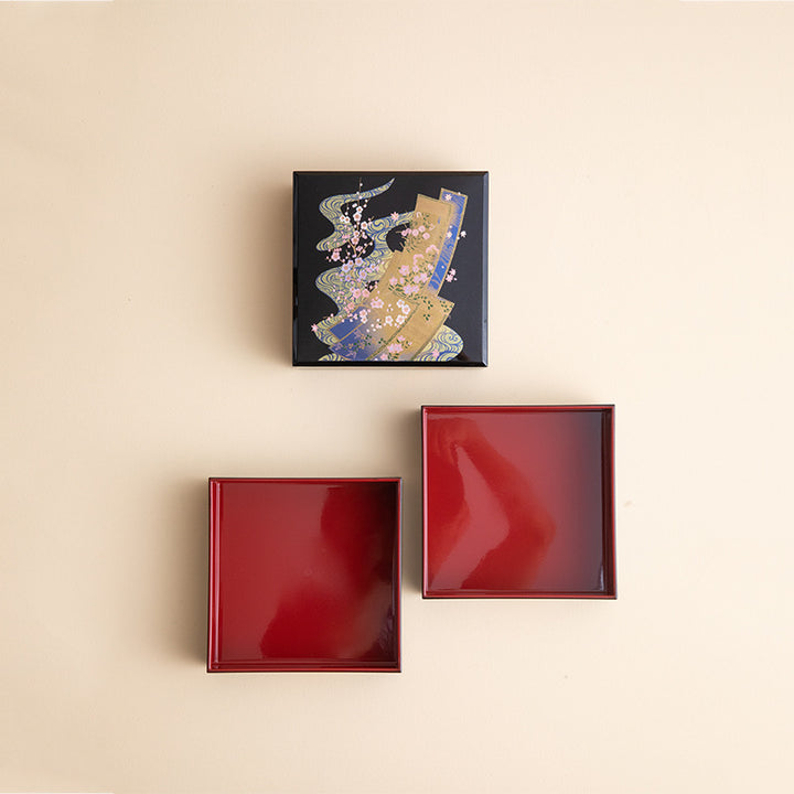 This image showcases the Oriental Heirloom: Japanese Lacquered Jewelry Box in its entirety. The box is open to reveal its deep, red lacquered interior, contrasted beautifully with the rich, dark exterior adorned with golden kimonos and cherry blossoms. The elegant craftsmanship is highlighted by the polished, glossy finish that reflects light subtly, emphasizing the intricate gold leaf details.