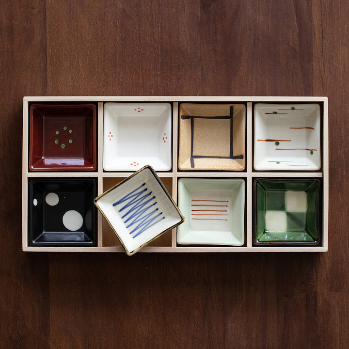 An overhead view of the complete set of 8 handcrafted Japanese Minoyaki side plates arranged in a wooden box. Each plate features a distinct design, showcasing the diverse and intricate patterns.