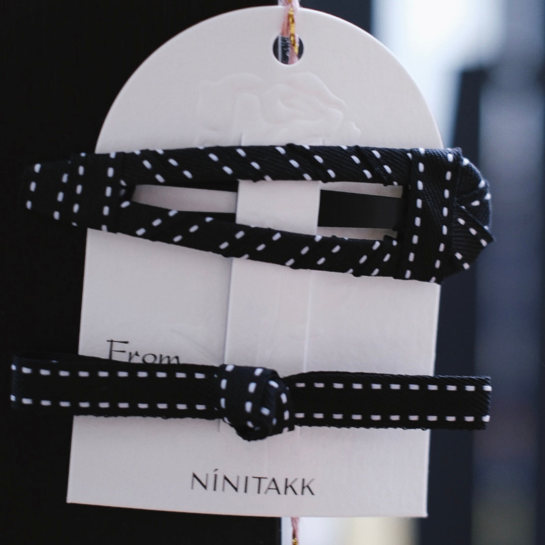 The set includes a sleek black fabric clip with delicate white stitched edges, paired with a matching black alligator clip adorned with a slim bow. Perfect for adding a touch of timeless elegance to any hairstyle.