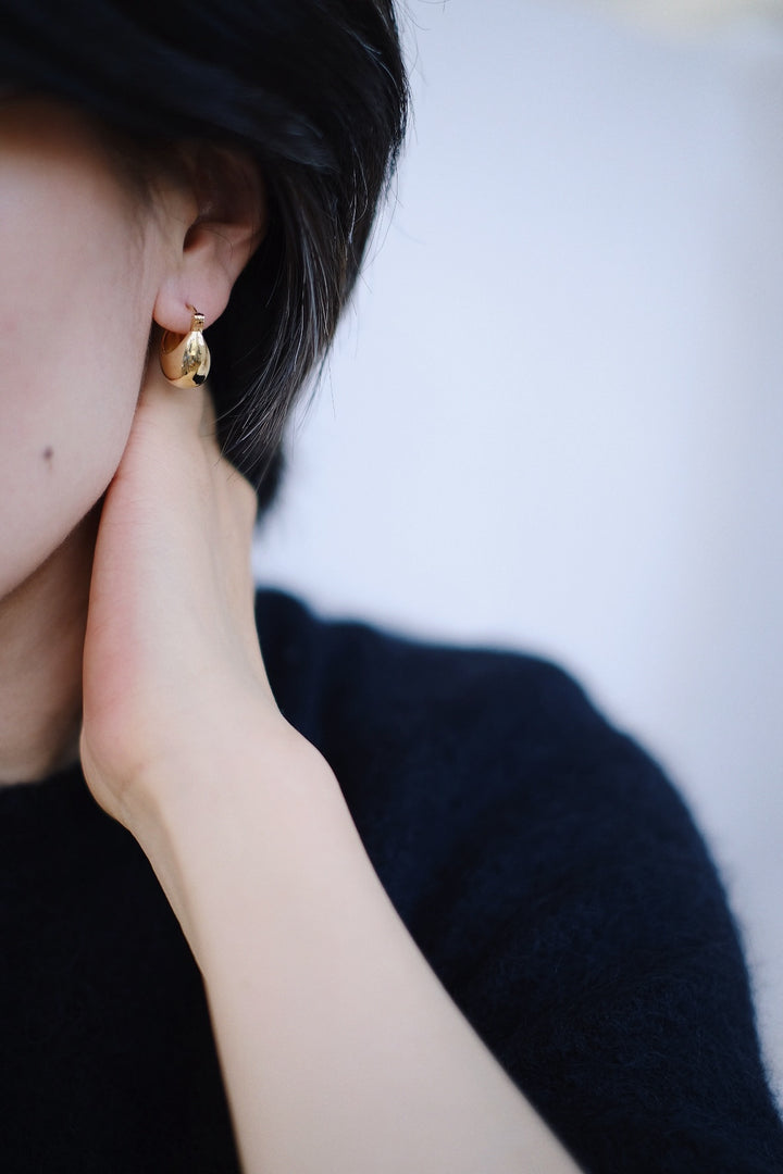 A model wearing the 18k gold-plated Vessel Earrings, showing off their warm, glowing finish and substantial look.