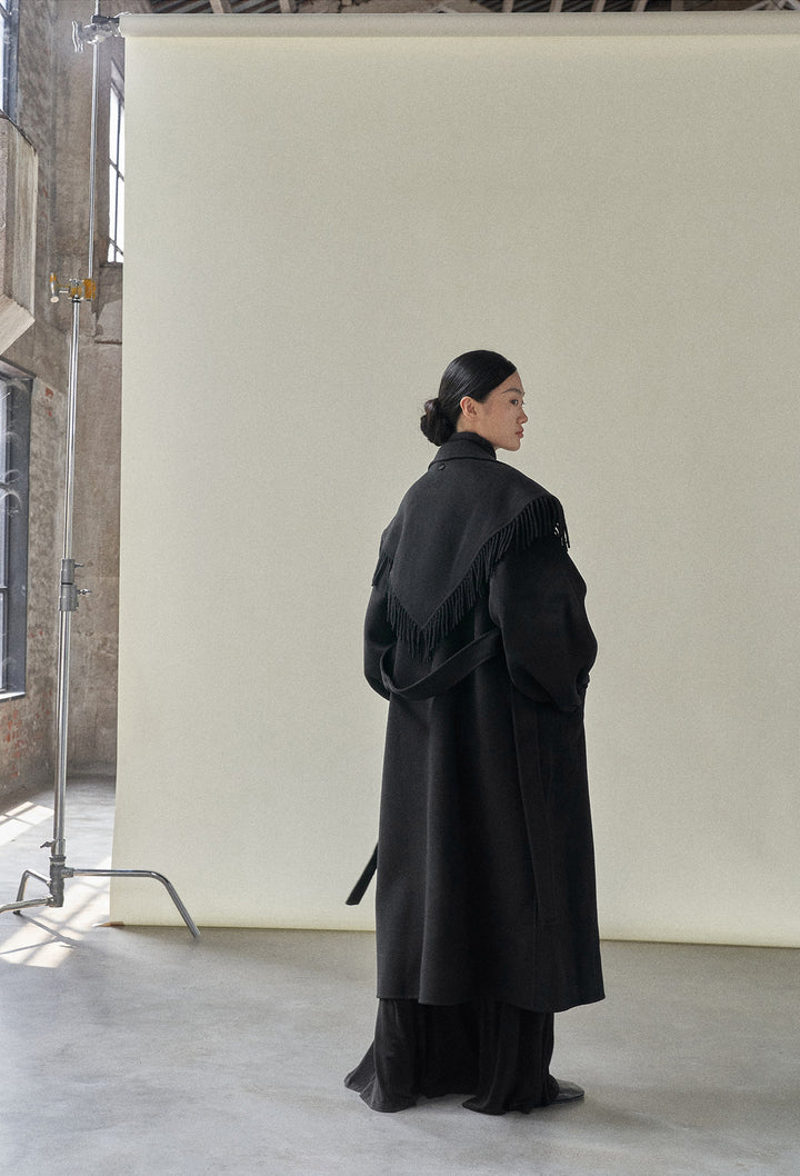 The back view of the black coat, showing the smooth, sleek design with the fringe scarf.