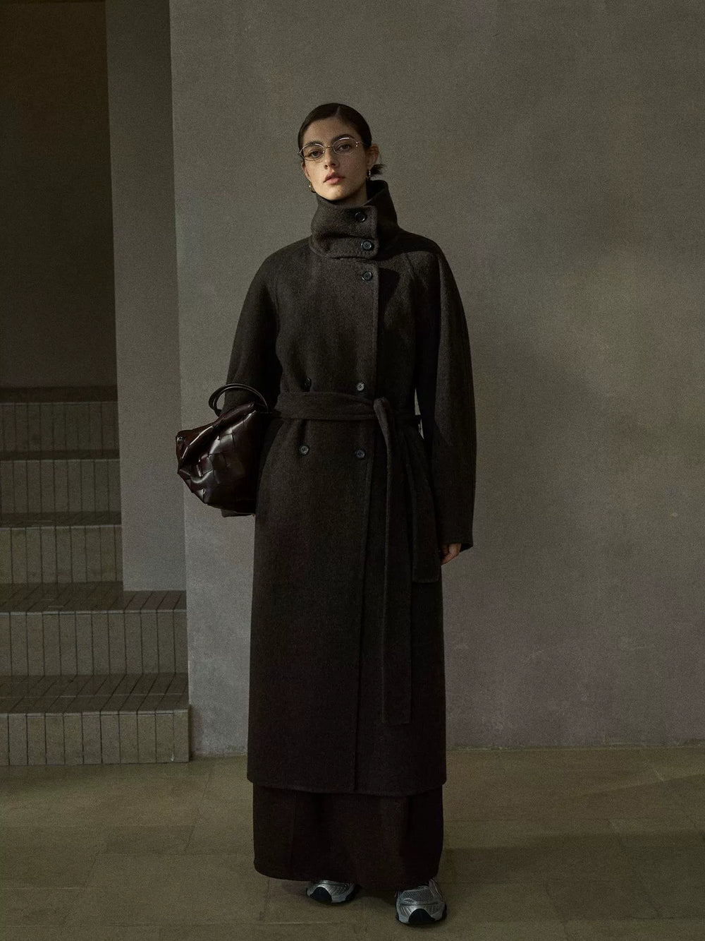 Model wearing chocolate brown wool coat with oversized collar, double-breasted button closure, and tie belt